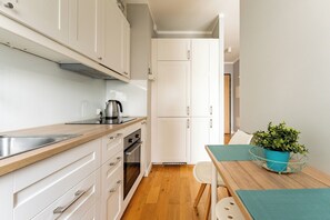Uma cozinha moderna com armários brancos, pia de aço inoxidável, chaleira e mesa de jantar com planta em vaso.