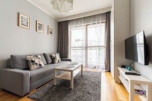 Ein modernes Wohnzimmer mit grauem Sofa, Couchtisch, Flachbildfernseher und gerahmten Bildern an der Wand.