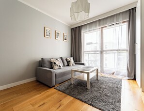 Uma sala de estar moderna com um sofá cinza, uma mesa de centro e uma grande janela com cortinas.