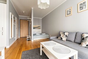 Una sala moderna con un sofá gris, una mesa de centro blanca y una cama con cabecero gris.