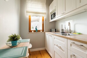Cocina compacta con microondas, pileta y alacenas. Se ve una ventana con vista a un balcón y una planta en maceta sobre la mesa.