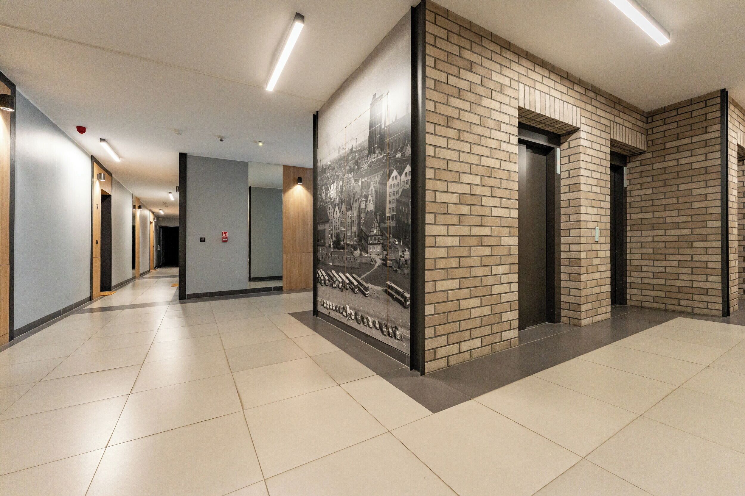 A modern hallway with a tiled floor, a large black-and-white photo on the wall, and a brick accent wall.