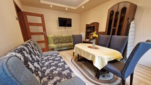 Un salon comprenant un canapé, des fauteuils, une table, un téléviseur et un meuble.