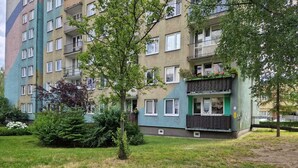 Un immeuble résidentiel à plusieurs étages, doté de balcons, d’un chemin pavé en briques et d’espaces verts.