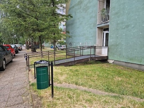 A building with a green exterior, a metal staircase leading to a door, and a parked car on the adjacent street.