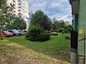 A residential area with parked cars, a building with a colorful mural, and a green lawn with bushes. - Romantica Comfort Apartment (Częstochowa)