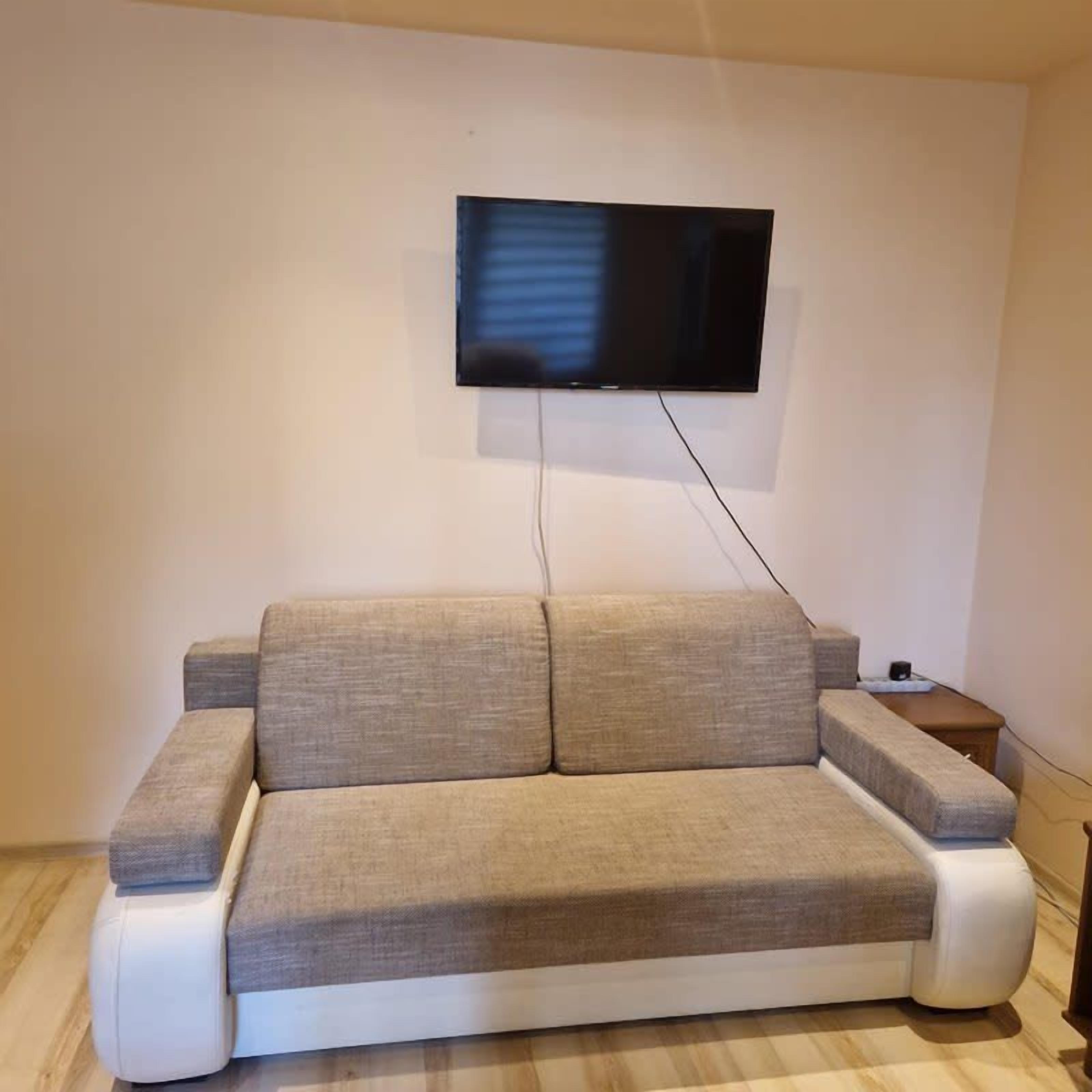 A modern living room with a sofa, a flat-screen TV mounted on the wall, and a small side table.