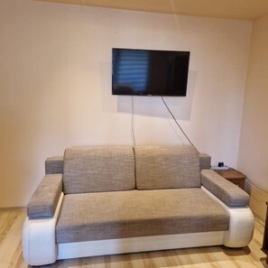 A modern living room with a sofa, a flat-screen TV mounted on the wall, and a small side table.