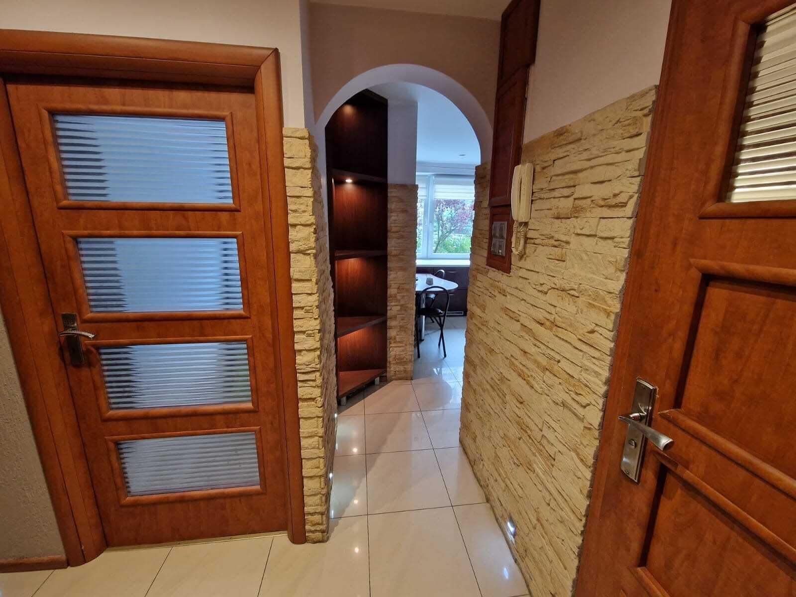 Un pasillo con puertas de madera, paredes de piedra y piso de baldosas.