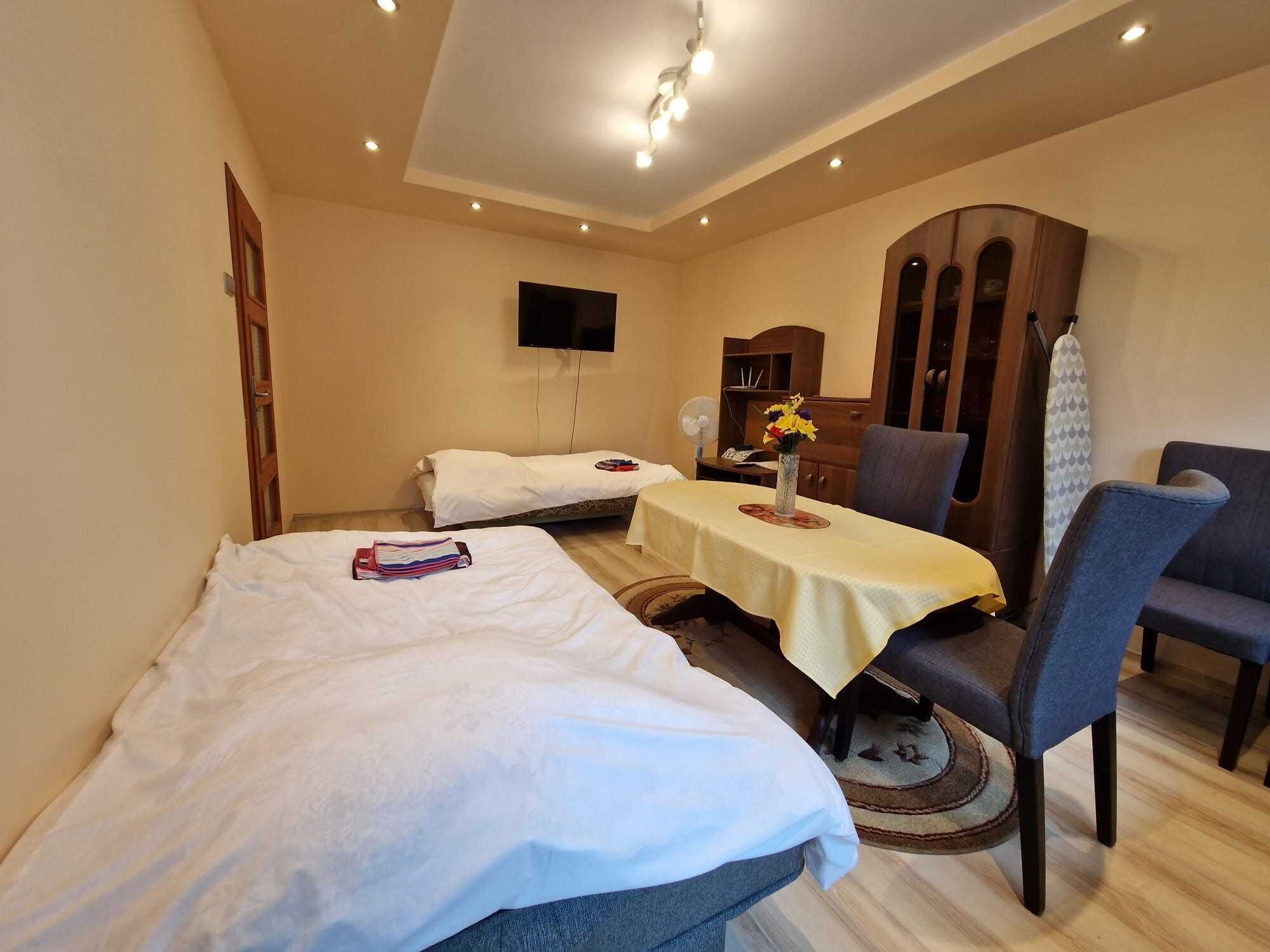 A hotel room with two beds, a dining table, a chair, a TV, and a wardrobe.