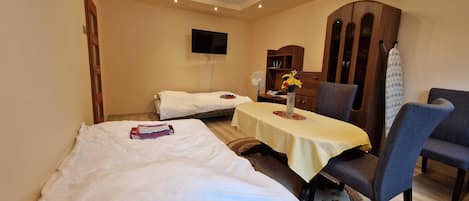 A hotel room with two beds, a dining table, a chair, a TV, and a wardrobe.