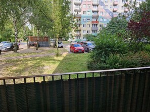 Ein Wohngebiet mit einer Reihe geparkter Autos, einer Grünfläche und einem mehrstöckigen Gebäude mit Balkonen im Hintergrund.