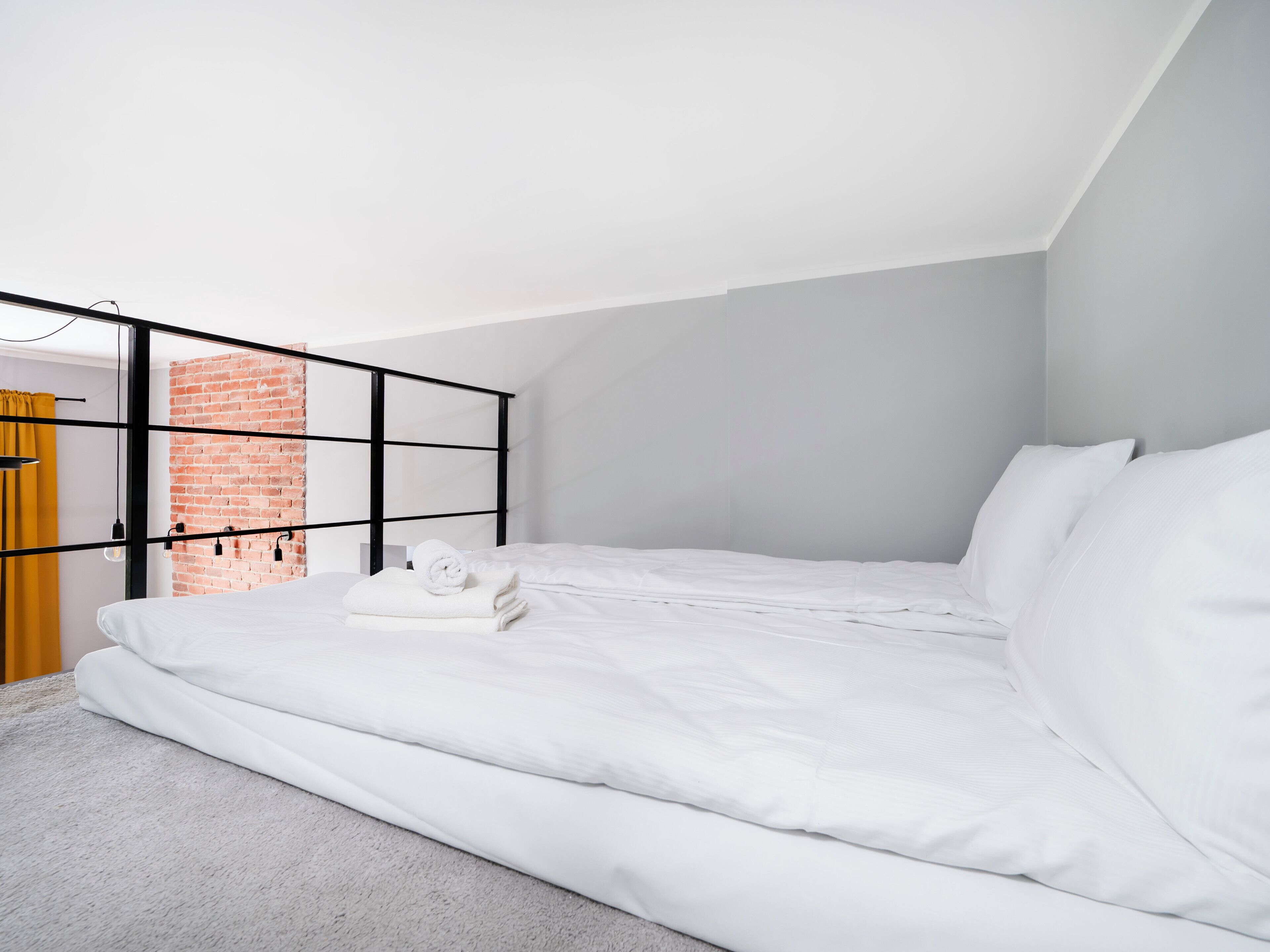 A modern bedroom with a white bed, a brick wall, and a black metal headboard.