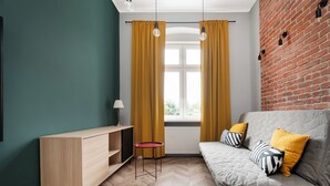 A modern living room with a sofa, a small table, a TV stand, and a window with curtains. - Nawrot City Center Studio (Łódź)
