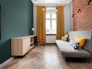 Ein modernes Wohnzimmer mit einer Couch, einem kleinen Tisch, einer TV-Konsole und einem Fenster mit Vorhängen.