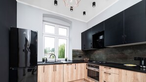A modern kitchen with a black refrigerator, wooden cabinets, a stainless steel stove, and a window with a view of greenery. - Nawrot City Center Studio (Łódź)