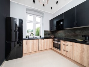 Eine moderne Küche mit einem schwarzen Kühlschrank, Holzschränken, einem Edelstahlherd und einem Fenster mit Blick auf Grünflächen.
