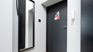 A hallway with a black door, a white wall, a mirror, a phone, and a colorful rug. - Nawrot City Center Studio (Łódź)