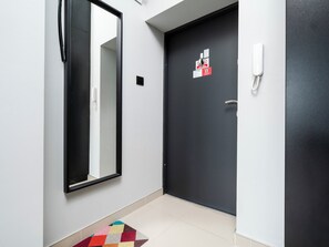 Ein Flur mit einer schwarzen Tür, einer weißen Wand, einem Spiegel, einem Telefon und einem farbenfrohen Teppich.