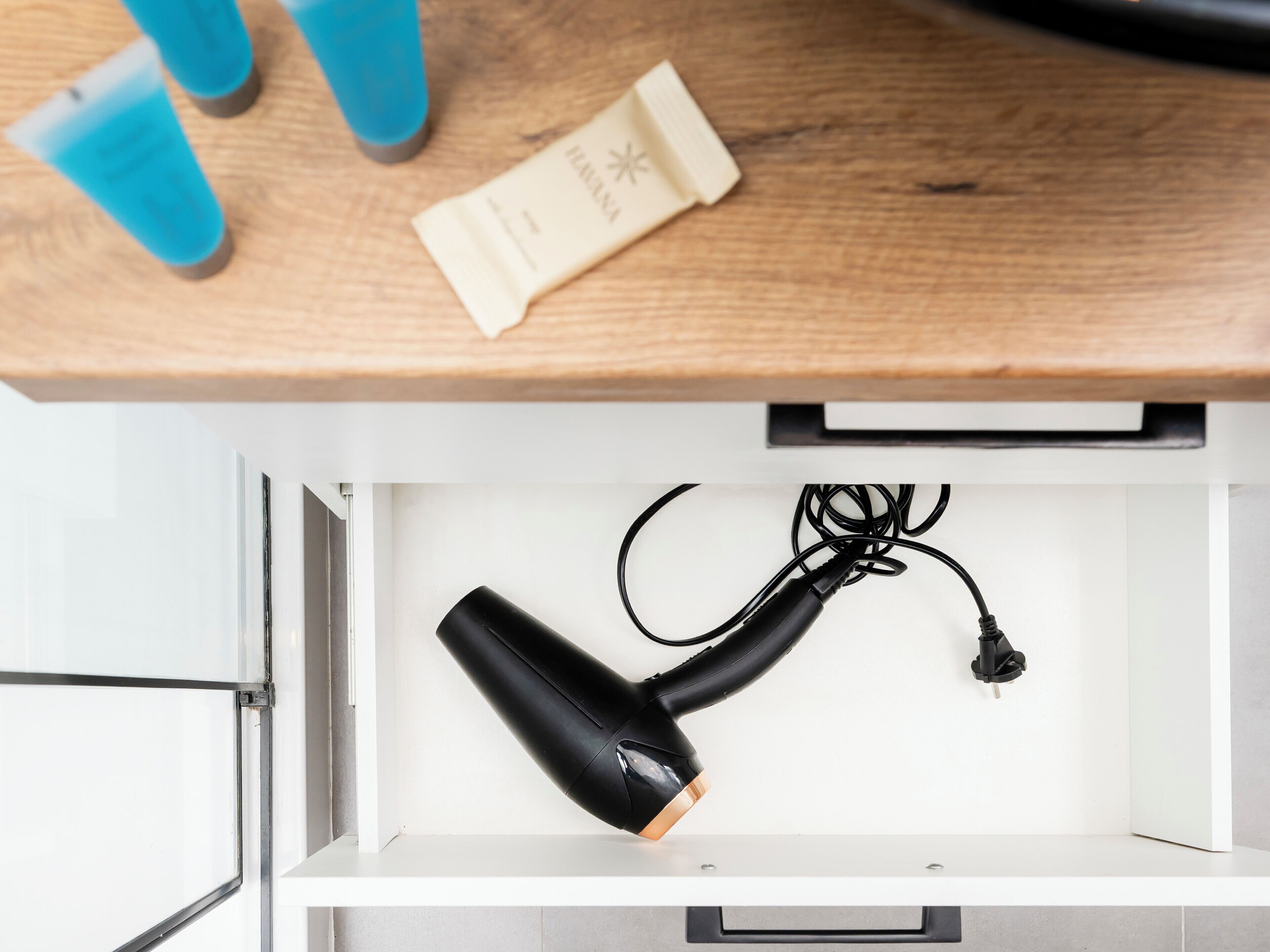 A drawer with a hairdryer and a blue container on a wooden surface.