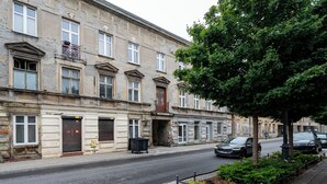 A street with historic buildings, a tree-lined sidewalk, and parked cars. - Nawrot City Center Studio (Łódź)