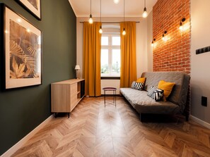 A modern living room with a herringbone wood floor, a grey sofa with striped cushions, a small side table, and a framed artwork on the wall. - Nawrot City Center Studio (Łódź)