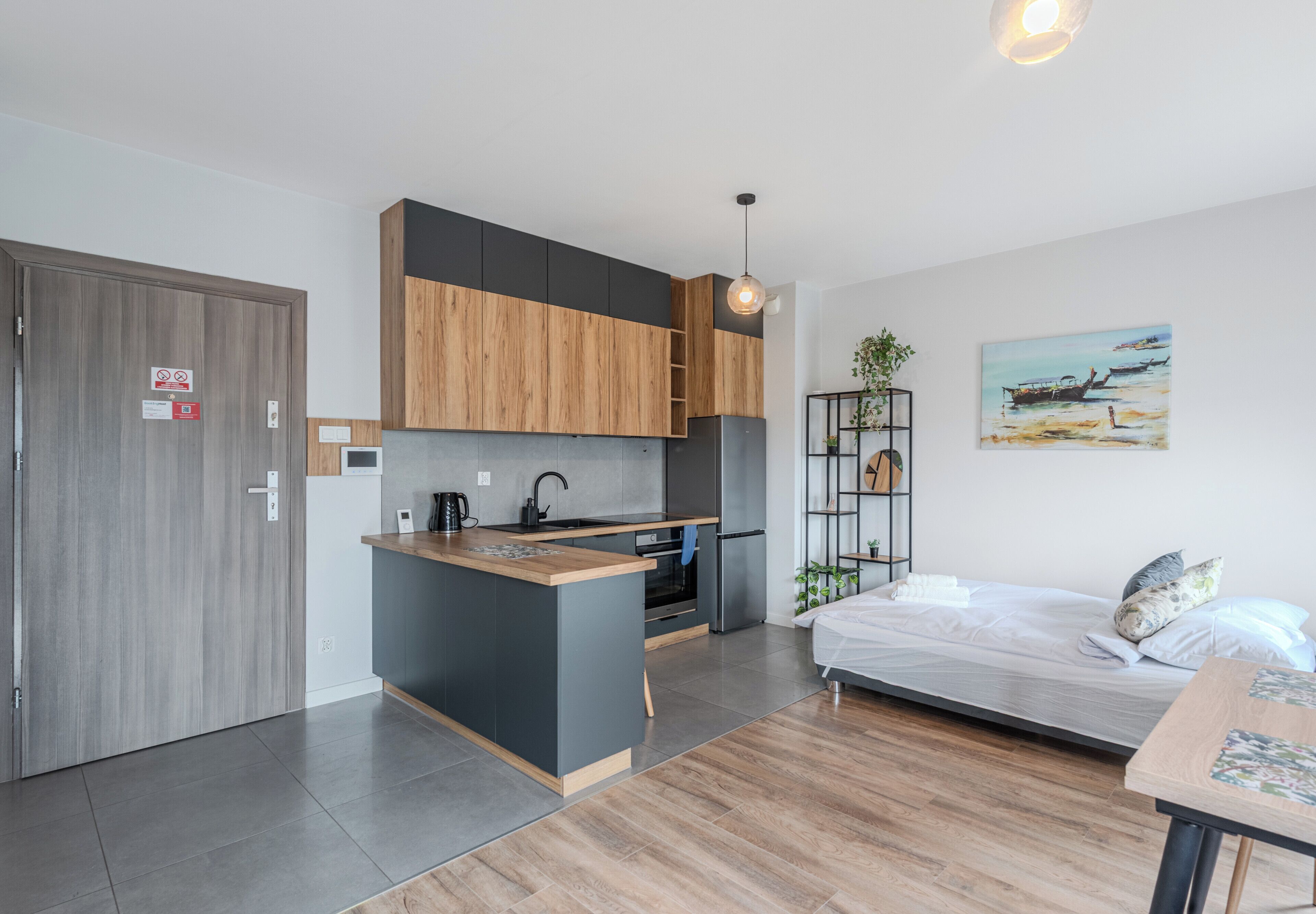A compact apartment with a kitchenette, a bed, a dining area, and a painting on the wall.