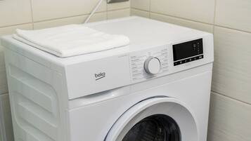 Een witte wasmachine met voorlader, een bedieningspaneel en een witte handdoek erbovenop.