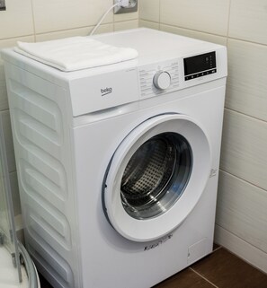 Een witte wasmachine met voorlader, een bedieningspaneel en een witte handdoek erbovenop.