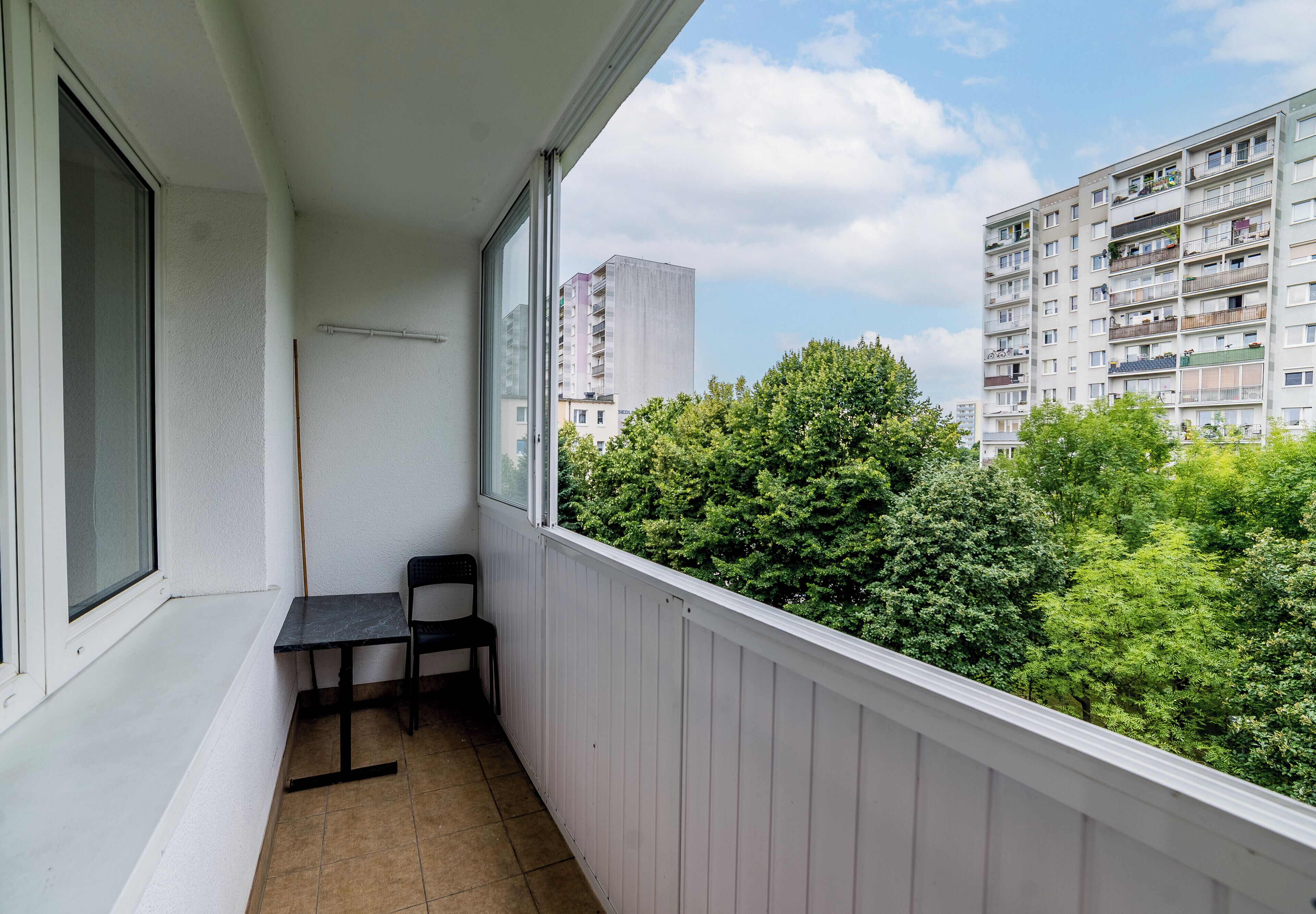 A balcony with a chair and a table, overlooking a building and trees.