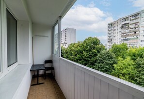 Ein Balkon mit Stuhl und Tisch, mit Blick auf ein Gebäude und Bäume.
