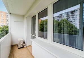 Ein Balkon mit weißem Heizkörper, einem Fenster und Blick auf ein mehrstöckiges Gebäude mit Balkonen.