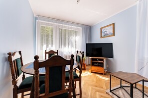A room with a dining table, chairs, a television, and a window with curtains. - Spadzista Comfort Apartment (Gdańsk)