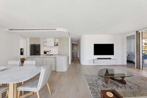 A modern living space with a kitchen, dining area, and a TV mounted on the wall. - 3BRM Oceanview Elegance (Gold Coast)