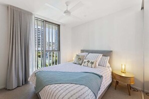 Ein Schlafzimmer mit einem Bett, einem Deckenventilator, einem Nachttisch und einem Fenster mit Vorhängen.