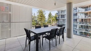 Ein moderner Essbereich im Freien mit Tisch und Stühlen, großen Fenstern und Blick auf ein Wohngebäude.