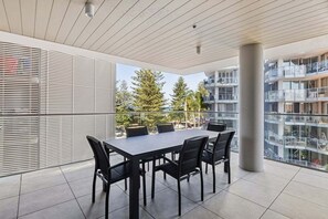 Ein moderner Essbereich im Freien mit Tisch und Stühlen, großen Fenstern und Blick auf ein Wohngebäude.