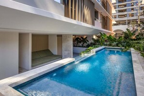 A modern hotel with a swimming pool, outdoor seating, and a view of adjacent buildings. - 3BRM Oceanview Elegance (Gold Coast)