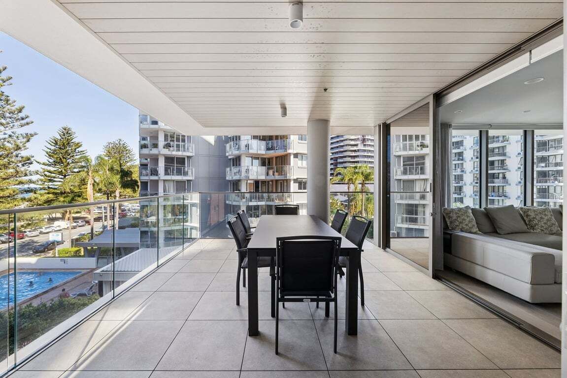 Un appartement moderne doté d’un balcon, d’un coin repas et offrant une vue sur d’autres immeubles et une piscine.