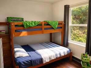 Una cama litera con un cojín de Minecraft color verde, una colcha a rayas y una ventana con cortinas.
