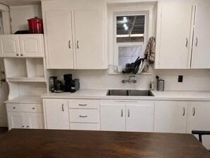 A kitchen with white cabinets, a wooden table, and a window above the sink.