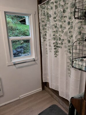 A bathroom with a window, a shower curtain with a leaf pattern, and a wooden bench.