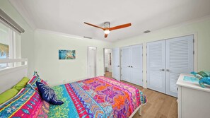 Een slaapkamer met een bed, een plafondventilator, witte kasten en een raam.