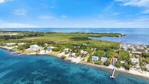An aerial view of a coastal area with clear blue waters, a pier, and several buildings surrounded by greenery. - Oceanfront Beach House 3BR|3BA Newly renovated (Marathon)