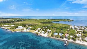An aerial view of a coastal area with clear blue waters, a pier, and several buildings surrounded by greenery. - Oceanfront Beach House 3BR|3BA Newly renovated (Marathon)