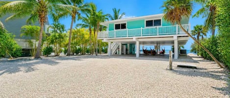A beachfront property with a covered patio, palm trees, and a view of the ocean.