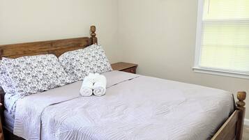 Een slaapkamer met een houten bedframe, een witte quilt en een kussen met bloemen.
