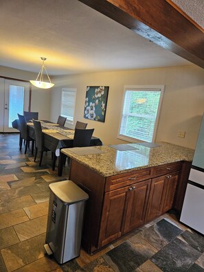 A kitchen with granite countertops, wooden cabinets, a stainless steel trash can, and a dining area with a table and chairs. - Delightful 3-bedroom house charming Garner nc close to Raleigh downtown (Garner)