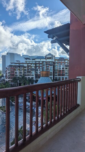 Uma varanda com vista para um complexo hoteleiro, incluindo uma área de piscina e edifícios com vários andares.