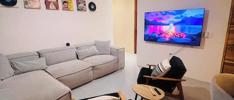 Una sala de estar con un sofá, una mesita, una silla, un ventilador de techo y un televisor que muestra una imagen panorámica.